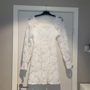 Vit blommig klänning - En vacker vit klänning med blommigt mönster och långärmad design. Perfekt för speciella tillfällen som t.ex student/skolavslutning. Klänningen har en normal passform, storlek M. Köpt från Pieces och är använd 1 gång och är kemtvättad efteråt. 