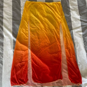 Orange och gul strandkjol - Snygg långkjol i en härlig ombre av orange och gul. Kjolen har slits på båda sidorna på framsidan som ger en extra touch. Perfekt för sommarens varma dagar. Materialet är lätt och luftigt.