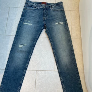 Jack and Jones jeans med slitningar - Snygga blå jeans med slitningar på framsidan från Jack and Jones, modellen är Tapared Mike. W30 L30. 