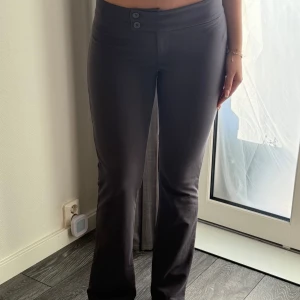 Gråa byxor med bootcut - Snygga gråa byxor med bootcut och låg midja. Byxorna har en stilren design med två knappar i midjan. Perfekta för en trendig look.