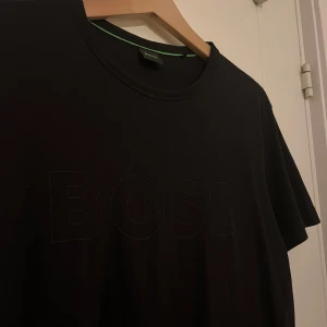 Svart t-shirt från Boss - Snygg svart t-shirt från Boss med diskret logga på bröstet. T-shirten har en normal passform. Hör av dig vid funderingar!