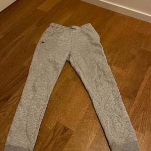 Grå mjukisbyxor från Lacoste  - Säljer ett par grå mjukisbyxor från Lacoste. Byxorna har en enkel design med resår i midjan och en liten logotyp på benet. 