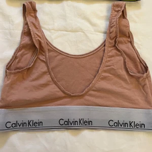 Beige linnetopp från Calvin Klein - Säljer en beige linnetopp från Calvin Klein med elastiskt band med logotypen i svart och vitt. Toppen har en bekväm passform och är perfekt för en avslappnad stil.