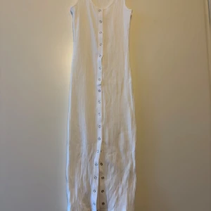 Vit ärmlös långklänning med knappar - Snygg vit långklänning i ribbat material med knappar framtill. Den är ärmlös och perfekt för varma dagar. Enkel och stilren design som passar till många tillfällen.