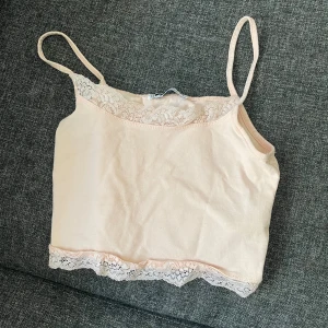 Linne med spetsdetaljer - Säljer ett gulligt linne med smala axelband och spetsdetaljer vid halsringning och nederkant.