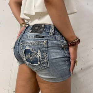 Missme jeans minishorts  - Snygga blå jeansshorts från Miss Me med slitna detaljer och coola broderade bakfickor. Shortsen en låg midjad passform, perfekt för sommaren.             Midjemått tvärs över: 35cm                         Längd: 23 cm                                                  Benöppning: 25cm