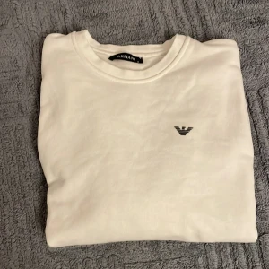 Vit tröja från Armani - Säljer en stilren vit tröja från Armani med deras ikoniska logga broderad på bröstet. Tröjan har en klassisk rund hals och är perfekt för en minimalistisk look. Passar bra till både jeans och chinos. Pris kan diskuteras vid snabb affär.
