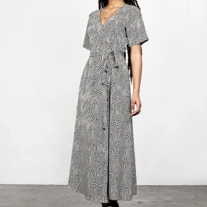 Svartvit mönstrad klänning från Disturbia - Säljer en unik svartvit klänning från Disturbia med ett iögonfallande mönster. Klänningen har korta ärmar och en v-ringad hals. Den är lång och har ett knytband i midjan för en smickrande passform. Perfekt för dig som vill sticka ut!