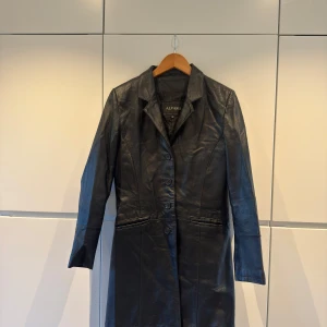 Svart skinnkappa - Snygg svart skinnkappa från Alvaro med knappar framtill. Perfekt för en stilren look. Kappan har långa ärmar och en klassisk krage. Kappan är knappt använd och har inga defekter. Pris kan diskuteras
