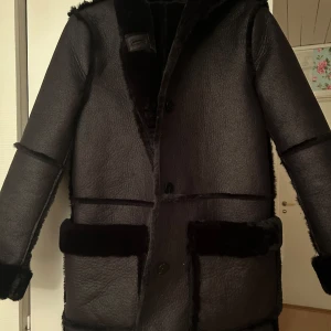 Svart pälsjacka med huva - Säljer en elegant svart reversible jacka med huva från Zara. Jackan har en stilren design med knappar framtill och är perfekt för kyliga dagar. Den är långärmad och har en mjuk, lyxig känsla. Strlk XS, säljer då den inte kommer till användning. 