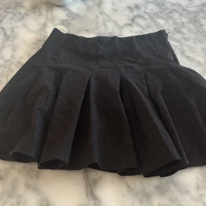 Svart kortkjol - Snygg svart kortkjol med veckad design. Perfekt för en stilren look. Kjolen har en klassisk passform och är lätt att matcha med olika toppar.