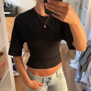 Svart croppad topp med knyt i ryggen - Säljer en svart croppad topp med korta ärmar och snygg knytning i ryggen. Toppen har en tight passform och är perfekt att styla med jeans eller kjol.