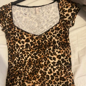 Leopardmönstrad topp från Nelly - Säljer en snygg leopardmönstrad topp från Nelly med v-ringning och korta ärmar. Toppen har svarta spetsdetaljer längs halsringningen och är i ett stretchigt material. Perfekt för dig som vill sticka ut lite extra!
