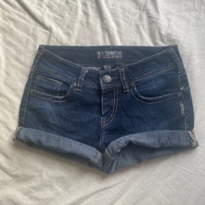 Lågmidjade jeansshorts - Snygga mörkblå jeansshorts från Silver med klassiska fem fickor och uppvikta benslut. Shortsen har kontrastsömmar och dekorativ broderad bakficka. Perfekta för varma dagar och enkel att matcha med olika toppar.