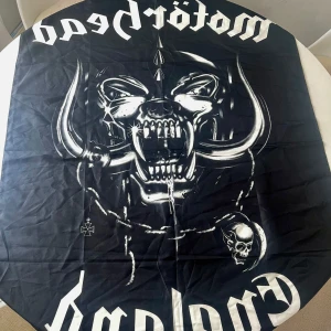 Svart flagga  med Motörhead-tryck - Svart flagga med stort vitt tryck av Motörhead-loggan och bandets ikoniska snubbe. Perfekt för dig som gillar rock. Har suttit på väggen hemma.