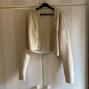 Beige croppad kofta från Zara - Säljer en beige croppad kofta från Zara med långa ärmar och rund halsringning. Koftan har knappar framtill och är stickad i ett mjukt material. Perfekt för lager-på-lager och enkel att matcha med olika outfits.