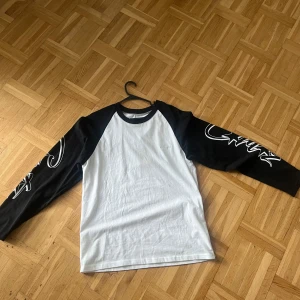 Corteiz Guerillaz långärmad tröja S - Säljer en svartvit långärmad tröja från Corteiz Guerillaz med coolt tryck på båda ärmarna. Tröjan har kontrastfärgade raglanärmar och rund halsringning. Tillverkad i mjuk bomull, perfekt för dig som gillar streetwear vibes.