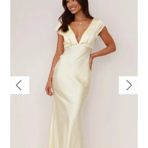 Gul långklänning i satin - Elegant långklänning i gul satin med djup v-ringning och korta ärmar. Klänningen har en snygg öppen rygg med twistad detalj och figurnära passform som ger en lyxig känsla. Perfekt för dig som vill sticka ut med en stilren look. Kommer från Billy J