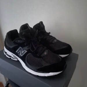 Svarta New Balance M2002 sneakers  - Säljer ett par svarta New Balance sneakers med vit sula och klassisk N-logga på sidan. Skorna har snörning och meshdetaljer för extra andningsförmåga. Perfekta för dig som gillar stilrena och sportiga skor. Och helt nya 