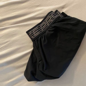 Svarta träningsshorts från Björn Borg - Säljer ett par svarta träningsshorts från Björn Borg med elastisk midja och diskret logga. Shortsen är lätta och bekväma, perfekta för gymmet eller löpning. Klassisk design med svart färg och randig resår.