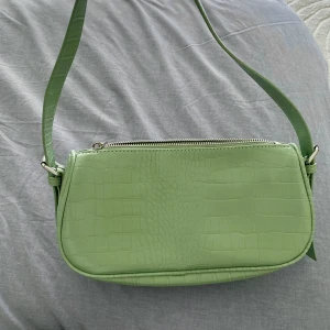 Ljusgrön liten handväska  - Liten enkel ljusgrön handväska som är perfekt om du vill ha lite mer färg till din outfit. Den har en dragkedja och även en ficka med dragkedja på insidan, bandet är justerbart