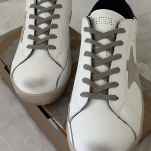 Vita sneakers från Golden Goose med grå detaljer - . Det var inte som jag hade tänkt mig så och jag råkade köpa för små storlek jag vill sälja dom för 1500kr priset går att diskuteras dom är helt äkta har köpt dom från golden gosse hemsida du får med dig box och väskan på sista bilden som är svart dom är helt oanvända 