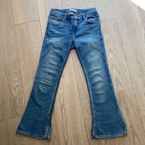 Blå bootcut jeans med slits från Zara - Säljer ett par blå bootcut/flare jeans från Zara med slits nertill på benen. Jeansen har klassisk femficksdesign, knapp och dragkedja i gylfen samt en snygg tvättad look. Använda bara ett fåtal gånger.