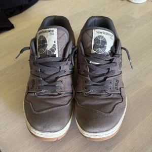 Mörkgråa New Balance 550 sneakers - Säljer ett par mörkgråa New Balance 550 sneakers med vita och bruna sulor. Skorna har snörning och är tillverkade i textil och syntetmaterial. Klassisk modell med rund tå och diskret logga på sidan. 