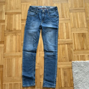 Blå skinny jeans från Vingino - Snygga blå skinny jeans från Vingino i storlek 14/164. Klassisk femficksmodell med dragkedja och knapp, samt coola slitningar och detaljer vid fickorna. Perfekta för dig som gillar en smal passform och stilren look.