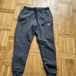 Grå mjukisbyxor från Hoodrich XS - Mörkgrå mjukisbyxor från Hoodrich i storlek XS. Byxorna har snörning i midjan, muddar vid bensluten och broderad logga på ena benet. Tillverkade i mjukt bomullsmaterial för maximal komfort. Perfekta för chill dagar eller streetwear-stil.