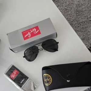 Svarta aviator-solglasögon från Ray-Ban - Snygga svarta aviator-solglasögon från Ray-Ban med klassisk tunn metallbåge och mörka linser. Kommer med originalfodral, putsduk och Ray-Ban-förpackning. Perfekt accessoar för soliga dagar.