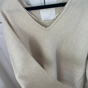 Beige stickad tröja med v-ringning från Samsa Collection - Mysig beige stickad tröja från Samsa Collection med v-ringad hals. Tröjan har lång ärm och en enkel, klassisk design som passar perfekt till många olika outfits. Kommer inte till användning. Skriv vid frågor 
