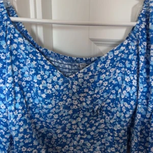 Blommig blå croppad blus - Säljer en blå croppad blus med vitt blommönster och långa puffärmar. Toppen har v-ringning och är perfekt för vår och sommar. Superfin att styla med jeans eller kjol! Dm mig om nu vill ha bilder med den på