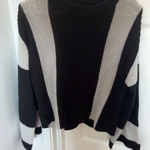 Svart och grå randig stickad tröja - Säljer en stickad tröja med utsvängda svarta och grå ränder. Tröjan har lång ärm, rund halsringning och är i ett mjukt, grovstickat material. Perfekt för kyligare dagar och enkel att matcha med jeans eller kjol.