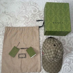 Beige keps från Gucci med GG-mönster - Säljer en beige keps från Gucci med klassiskt GG-mönster över hela kepsen. Justerbar rem baktill i brunt läder och detaljer i canvas. Kepsen levereras med originalpåse, box och tags.