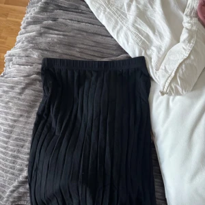 Svart ribbad kjol - Säljer en svart ribbad kjol med stretchig midja. Kjolen har en rak passform och är enkel att matcha med olika toppar. Perfekt för dig som gillar en stilren look.