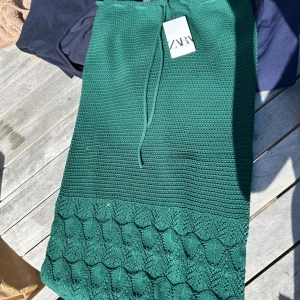 Grön stickad kjol från Zara - Säljer en grön stickad kjol från Zara med dragsko i midjan. Kjolen har ett snyggt mönster nertill och är perfekt för dig som gillar en unik och trendig stil. Passar till många olika looks och är superbekväm.