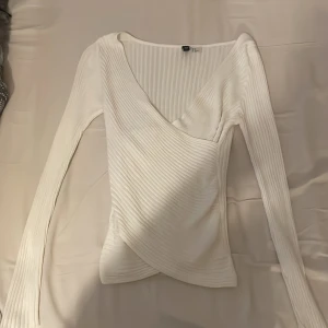 Vit ribbad omlottopp från H&M - Säljer en vit ribbad omlottopp från H&M i storlek XS. Toppen har lång ärm, v-ringning och omlottdesign framtill. Materialet är stretchigt och bekvämt, perfekt för att skapa en stilren look. Finns en liten fläck på toppen men går säkert att få bort☺️