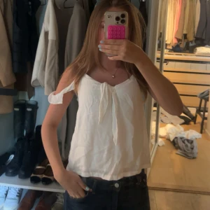 Vit linnetopp med knytband - Säljer en söt vit linnetopp med knytband framtill och smala axelband. Toppen är från Hollister och är i strl S. 