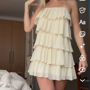 Ljus volangklänning med tunna axelband - Supersöt kort klänning i gul med flera lager plisserade volanger och tunna axelband. Den har en luftig och flowy känsla, perfekt för sommarens varma dagar. Klänningen är ärmlös och har en romantisk vibe som verkligen sticker ut.