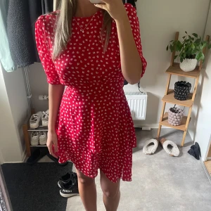 Röd blommig kortklänning med volang - Säljer en duperfin röd kortklänning med vita småblommor. Från Adoore