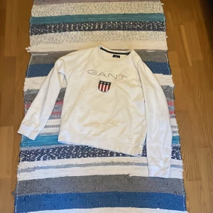 Vit sweatshirt från GANT med logo - Vit sweatshirt från GANT med broderad logotyp och sköld på bröstet. Klassisk rund halsringning och långa ärmar. Perfekt för dig som gillar en clean och sportig stil.