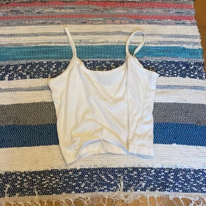 Vit ribbad linnetopp - Säljer en enkel och fräsch vit ribbad linnetopp med smala axelband. Perfekt för varma dagar eller att styla lager på lager. Toppens material är mjukt och stretchigt för en bekväm passform.