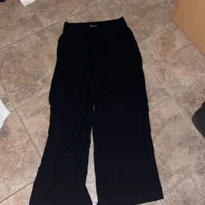 Svarta wide byxor från Gina Tricot - Svarta byxor från Gina Tricot i storlek 36. De har en relaxed wide fit, resår i midjan och snörning framtill. Perfekta för en chill och stilren look. Lätta och sköna, passar till allt.