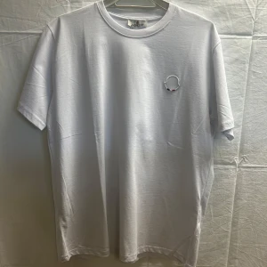 Vit Moncler t-shirt med broderad logga - Clean vit t-shirt från Moncler i bomull med broderad logga på bröstet och diskret Moncler-broderi på ärmen. Klassisk rund hals och korta ärmar, perfekt för en stilren och enkel look.