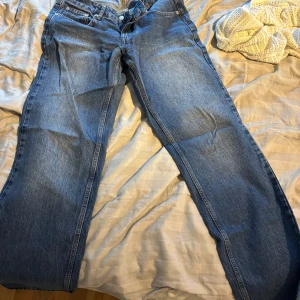 Blå raka jeans i klassisk modell - Säljer ett par blå jeans med rak passform och klassisk femficksdesign. Jeansen har normal midja och är tillverkade i slitstarkt denimtyg. Perfekta för en avslappnad och tidlös stil.