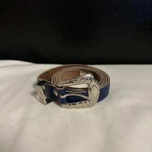 Blått bälte med silverdetaljer - Snyggt blått bälte med dekorativt silverspänne. Perfekt för att ge en extra touch till din outfit. Inga tecken på användning 