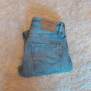 Ljusblå jeans från Jack & Jones - Säljer ett par klassiska ljusblå jeans från Jack & Jones. Jeansen har rak passform, fem fickor och bälteshällor. Tillverkade i bomull med snygg tvättad look och traditionell jeansknäppning. Perfekta för en avslappnad stil.