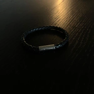 Skultuna Armband, flätat äkta läder  - Stilrent svart armband i flätat skinn med ett silverfärgat magnetlås från Skultuna. Perfekt accessoar för en modern look. Låset har diskret gravyr med varumärket.