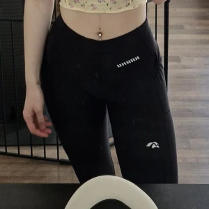 Svarta tights från Karhu - Säljer ett par svarta tights från Karhu med hög midja och praktisk ficka på sidan. Byxorna är tillverkade i stretchigt material med 88% polyester och 12% elastan, perfekta för träning eller en aktiv vardag.